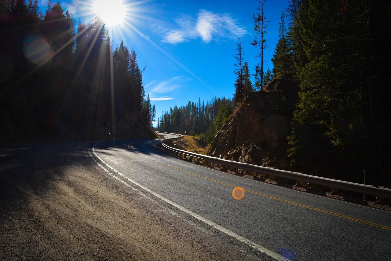 Scenic, winding mountain road bathed in sunlight, surrounded by tall pine trees under a vibrant blue sky. Scenic, winding mountain road bathed in sunlight, surrounded by tall pine trees under a vibrant blue sky.