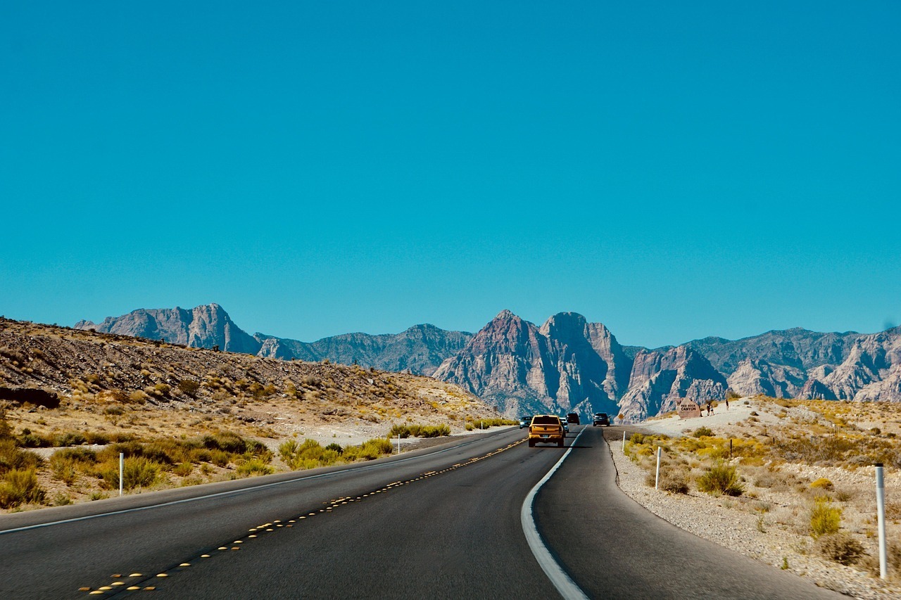 A car cruises down a desert highway with rugged mountains ahead—perfect timing for a Montana car title transfer. A car cruises down a desert highway with rugged mountains ahead—perfect timing for a Montana car title transfer.