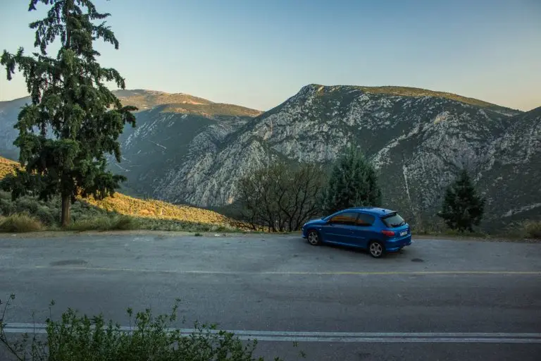Blue SUV parked on a roadside overlook with a mountainous landscape and valley in the background