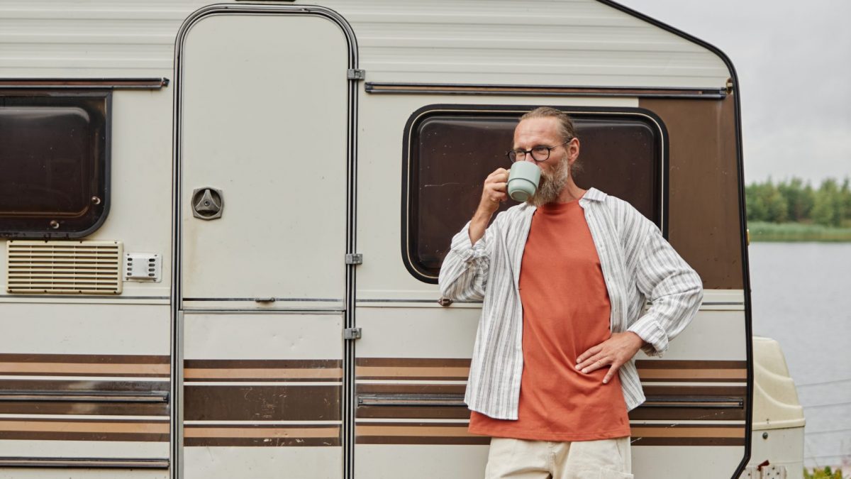 Vertical full length portrait of modern senior man enjoying cup of coffee standing by van outdoors in nature